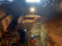 Un chercheur casqué se tient dans une immense fosse creusée dans le sol d'une grotte, entouré d'équipements archéologiques.