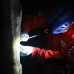 Photo d'un chercheur muni d'une lampe frontale échantillonnant une stalagmite dans une grotte.