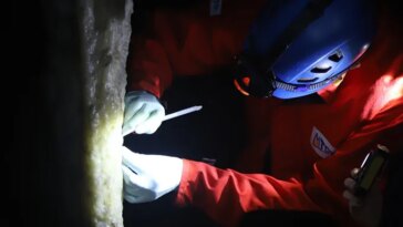 Photo d'un chercheur muni d'une lampe frontale échantillonnant une stalagmite dans une grotte.