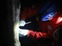 Photo d'un chercheur muni d'une lampe frontale échantillonnant une stalagmite dans une grotte.