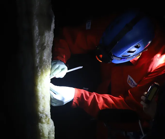 Dans les grottes peintes, l’ADN humain ancien s’accroche aux murs Photo d'un chercheur muni d'une lampe frontale échantillonnant une stalagmite dans une grotte.