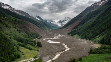 Une coulée de boue géante remplit une vallée entre deux montagnes en Suisse. Des montagnes enneigées sont visibles au fond et quelques débris au premier plan.
