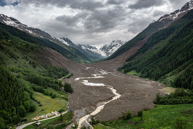 Une coulée de boue géante remplit une vallée entre deux montagnes en Suisse. Des montagnes enneigées sont visibles au fond et quelques débris au premier plan.