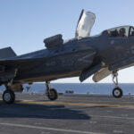 An F-35B Lightning II of Air Test and Evaluation Squadron 23 (VX-23) on the flight deck of JS Kaga (DDH-184) during F-35B developmental testing off Southern California, October 2024. US Navy photo by Dane Wiedmann, public domain, modified, https://commons.wikimedia.org/wiki/File:F-35B_launches_from_JS_Kaga_during_sea_trials-2.jpg