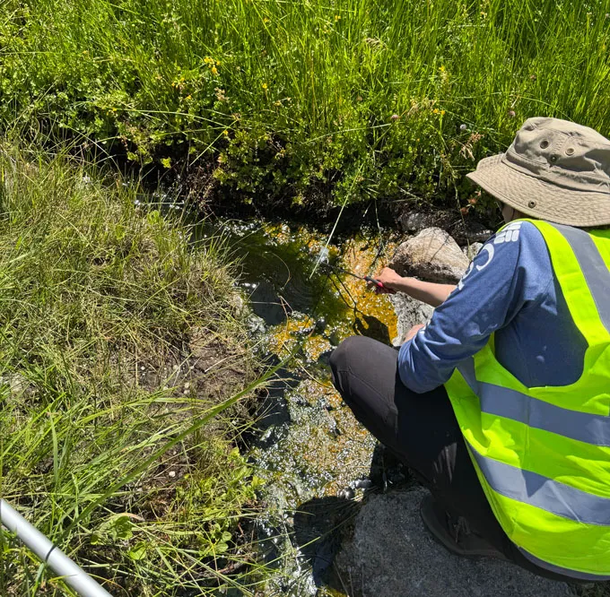 Rencontrez «l'amibe de feu», une survivante record de la chaleur extrême Une personne portant un gilet jaune vif s’accroupit près d’une source chaude pour prélever un échantillon d’eau.